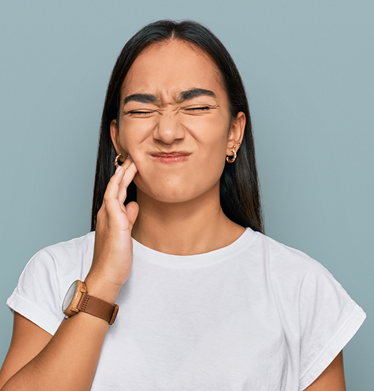 Woman holding her cheek in pain before seeing an emergency dentist in Maple Valley