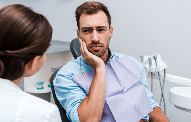 Man holding his cheek in pain while listening to his dentist