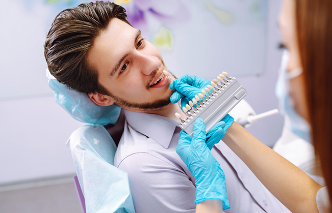 Cosmetic dentist holding a veneer to a patient's smile