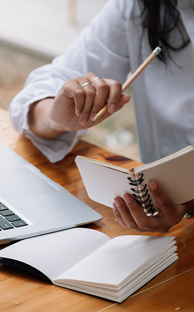 Woman holding a pencil and a notebook at a desk