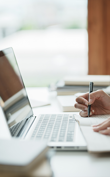 Person taking notes in front of a laptop